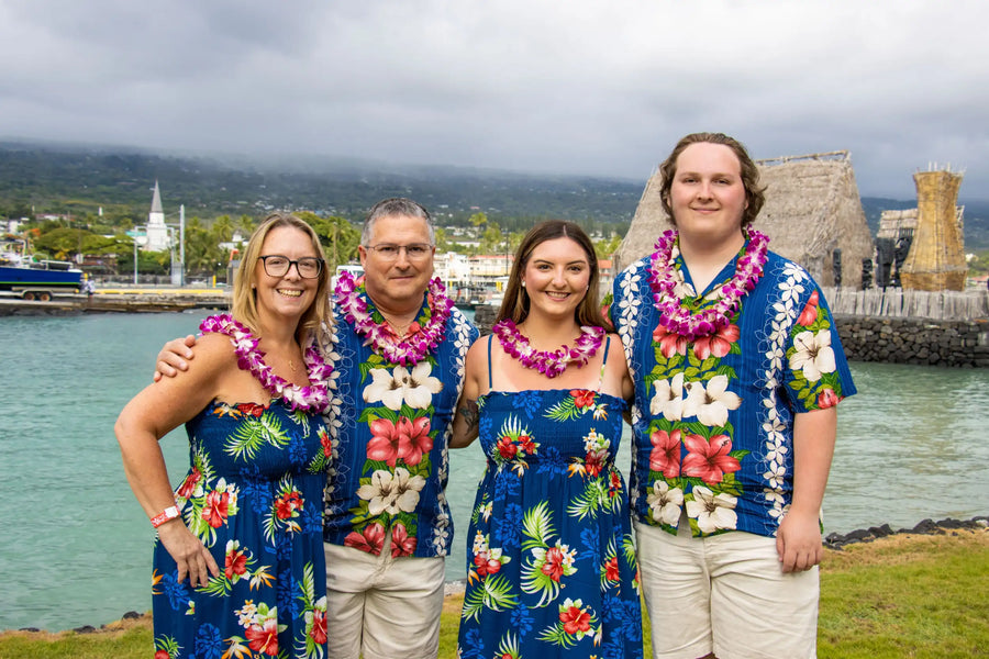 The family wears matching blue floral aloha shirts and dresses adorned with vibrant pink, red, and white tropical flowers.